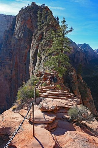 a line of hikers clinging to the chains, the canyon dropping away below a line of hikers clinging to the chains, the canyon dropping away below