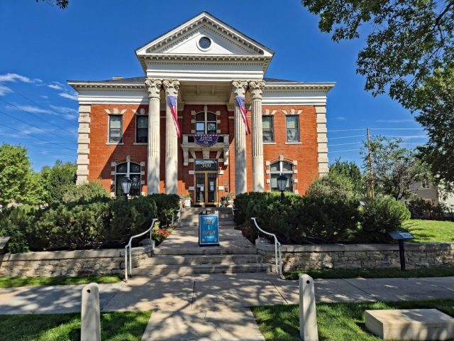 Historischer Prachtbau in Cheyenne: Die Old Governors' Mansion Das Bild zeigt die symmetrische, im Colonial-Revival-Stil erbaute Frontfassade der historischen Gouverneursvilla aus roten Backsteinen unter strahlend blauem Sommerhimmel. 1000