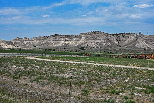 nz7 9001Panoramic View of the National Monument – Historic farm machinery in the barren prairie grass with the silhouette of Dome Rock in the background. nz7 9001