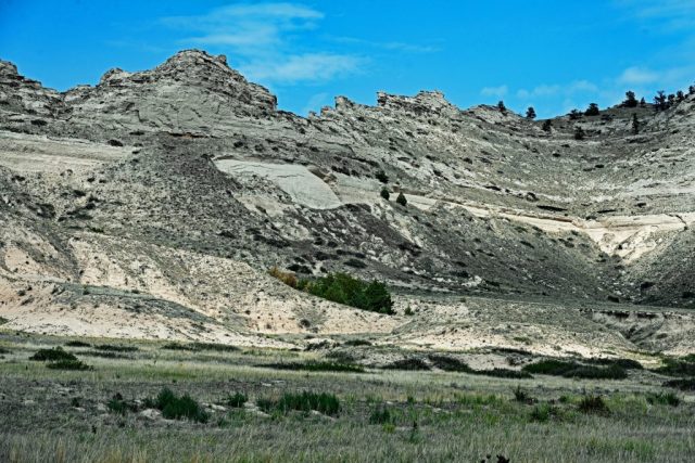 View into the Amphitheater of the Cliffs – The heavily eroded sediment slopes of the Brule Formation with a green cluster of trees in the valley. nz7 9004